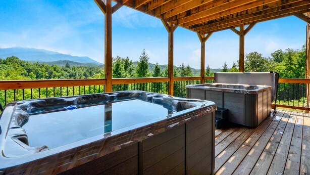 Een houten terras met twee whirlpools en een pergola.