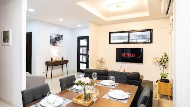 A modern living room with a dining area, a TV mounted on the wall, and a cozy seating arrangement. - 3bd Lux City Oasis LAS Pinas (Las Pinas)