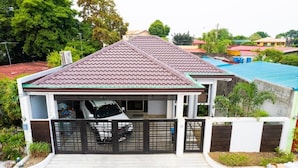 A residential house with a tiled roof, a garage with a black gate, and a small garden area. - 3bd Lux City Oasis LAS Pinas (Las Pinas)