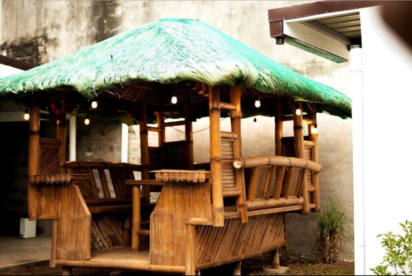 Una estructura de madera con techo de paja y zona de estar, probablemente un quiosco o espacio para sentarse al aire libre.