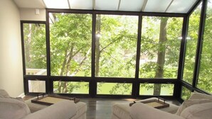 A room with two white sofas, a large window with a view of trees, and a wooden floor. - Lakefront with kayaks and private dock.  Pet friendly, nearby dog park (Hot Springs Village)