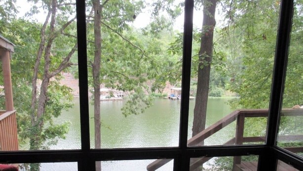 A room with a large window overlooking a lake, a wooden deck, and a patterned rug. - Lakefront with kayaks and private dock.  Pet friendly, nearby dog park (Hot Springs Village)