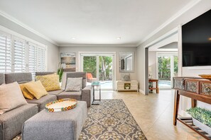 Ein geräumiges Wohnzimmer mit einer grauen Sofagarnitur, einem gemusterten Teppich und einem Holztische.