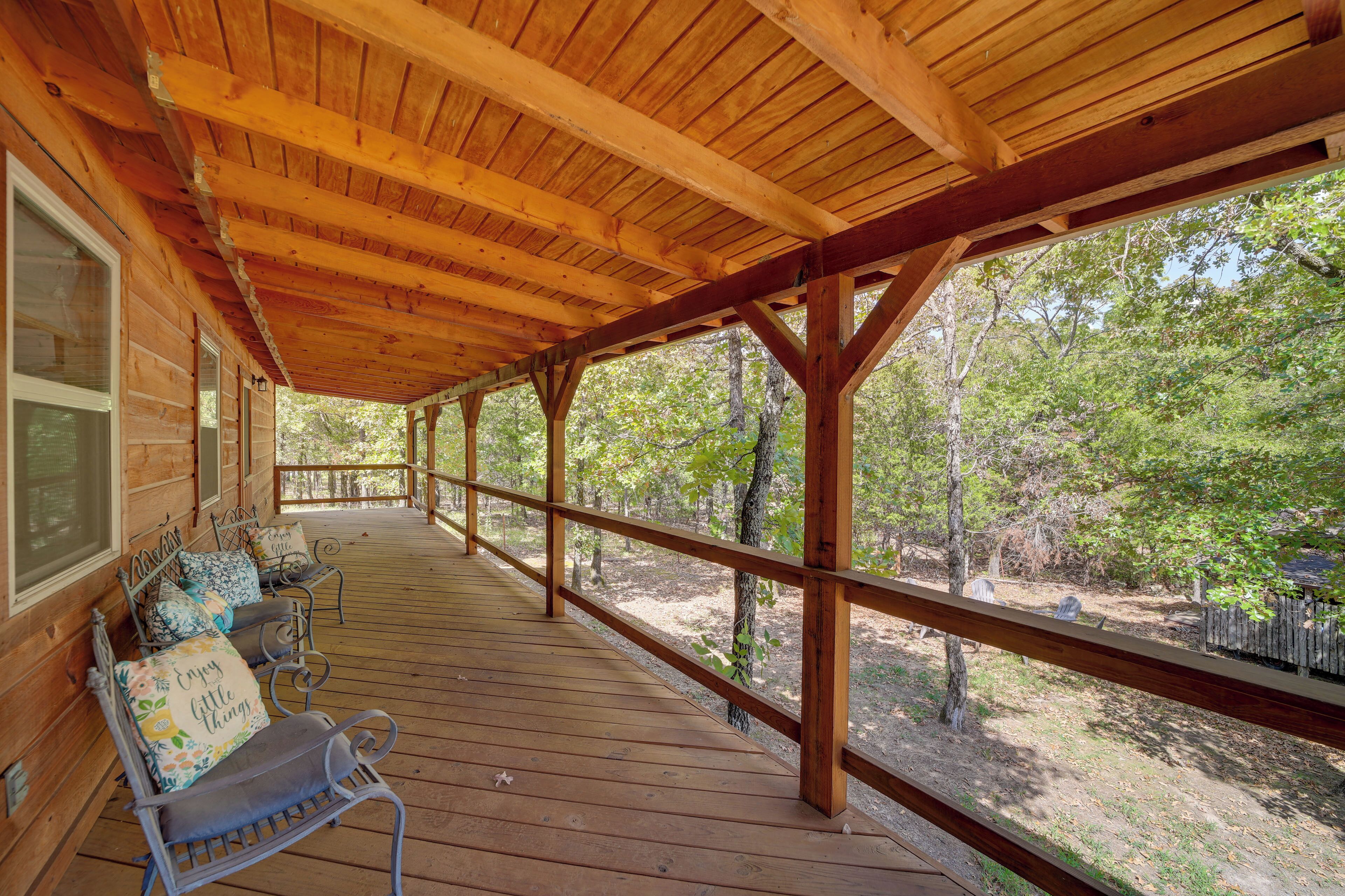 A covered wooden deck with benches and a railing, overlooking a wooded area.