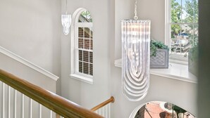 A staircase with a wooden handrail, a chandelier, and a window with a view of the outside. - Spacious & Modern Pool Retreat Near DFW Metroplex! (Grand Prairie)