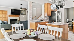 A modern kitchen with wooden cabinets, a central island, and a dining area with a table set for four. - Spacious & Modern Pool Retreat Near DFW Metroplex! (Grand Prairie)