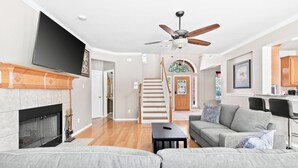 A modern living room with a fireplace, a sofa, a television, and a staircase leading to another room. - Spacious & Modern Pool Retreat Near DFW Metroplex! (Grand Prairie)