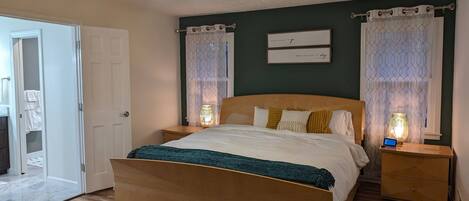 A bedroom with a wooden bed, two bedside tables with lamps, a ceiling fan, and a door leading to a bathroom.