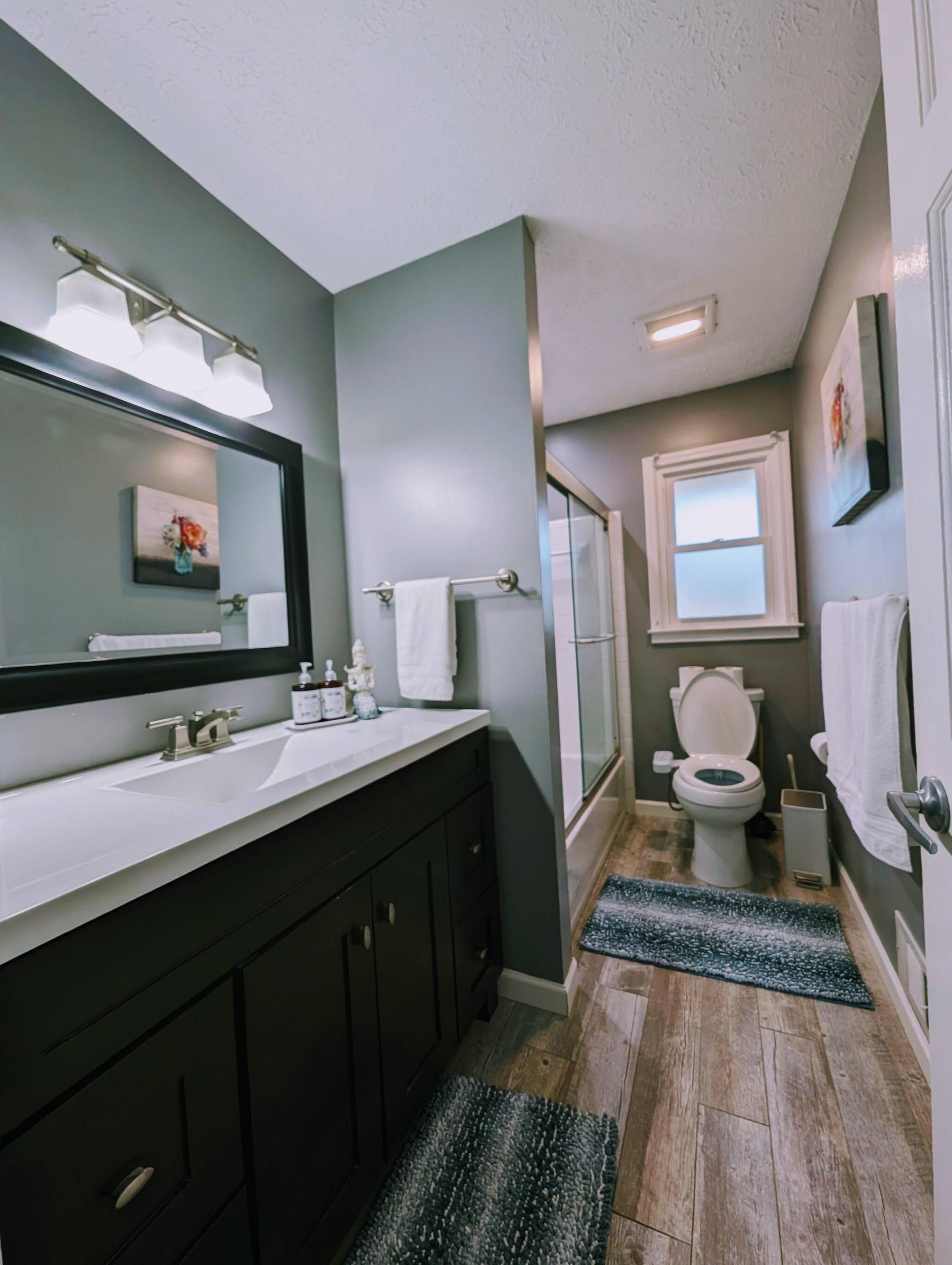A bathroom with a double vanity, a toilet, a shower, and a small window.