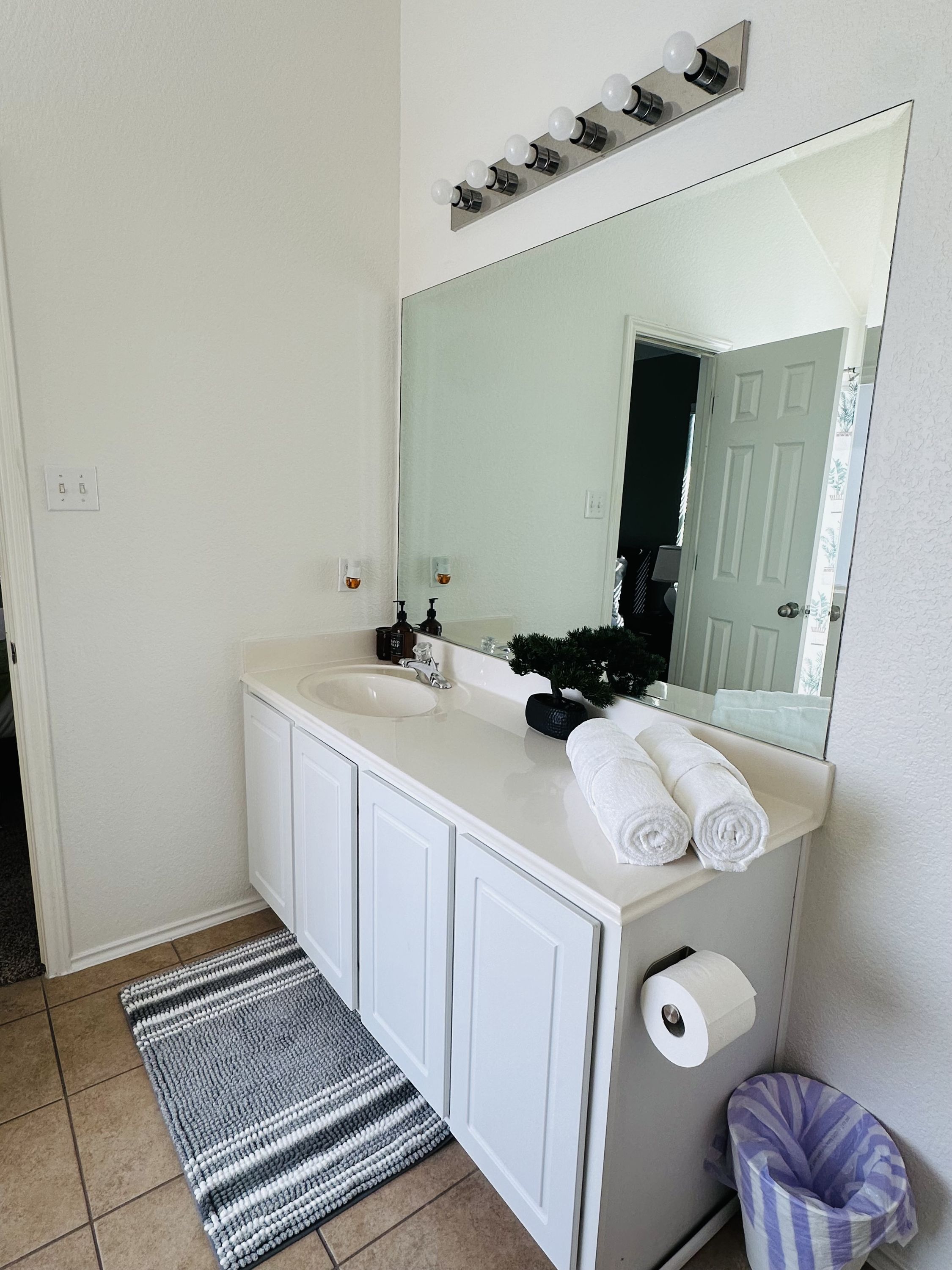 A bathroom with a white vanity, a large mirror, a towel rack, and a striped rug.