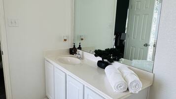 A bathroom with a white vanity, a large mirror, a towel rack, and a striped rug.