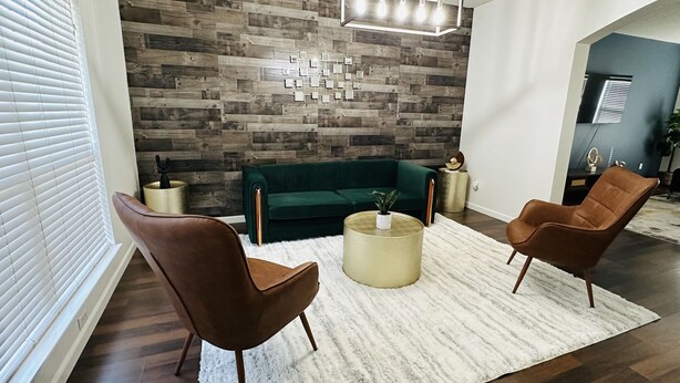 Una sala de estar moderna con un sofá verde, dos sillones marrones, un felpudo blanco y una pared de madera con un diseño geométrico.