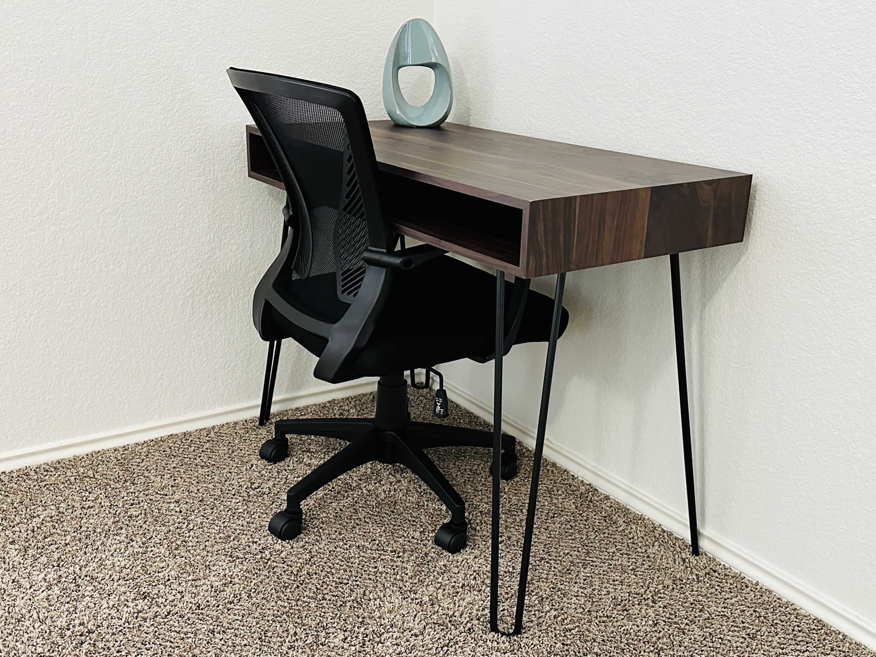 Una moderna silla de oficina con respaldo de malla y un escritorio de madera oscura de diseño elegante y minimalista.