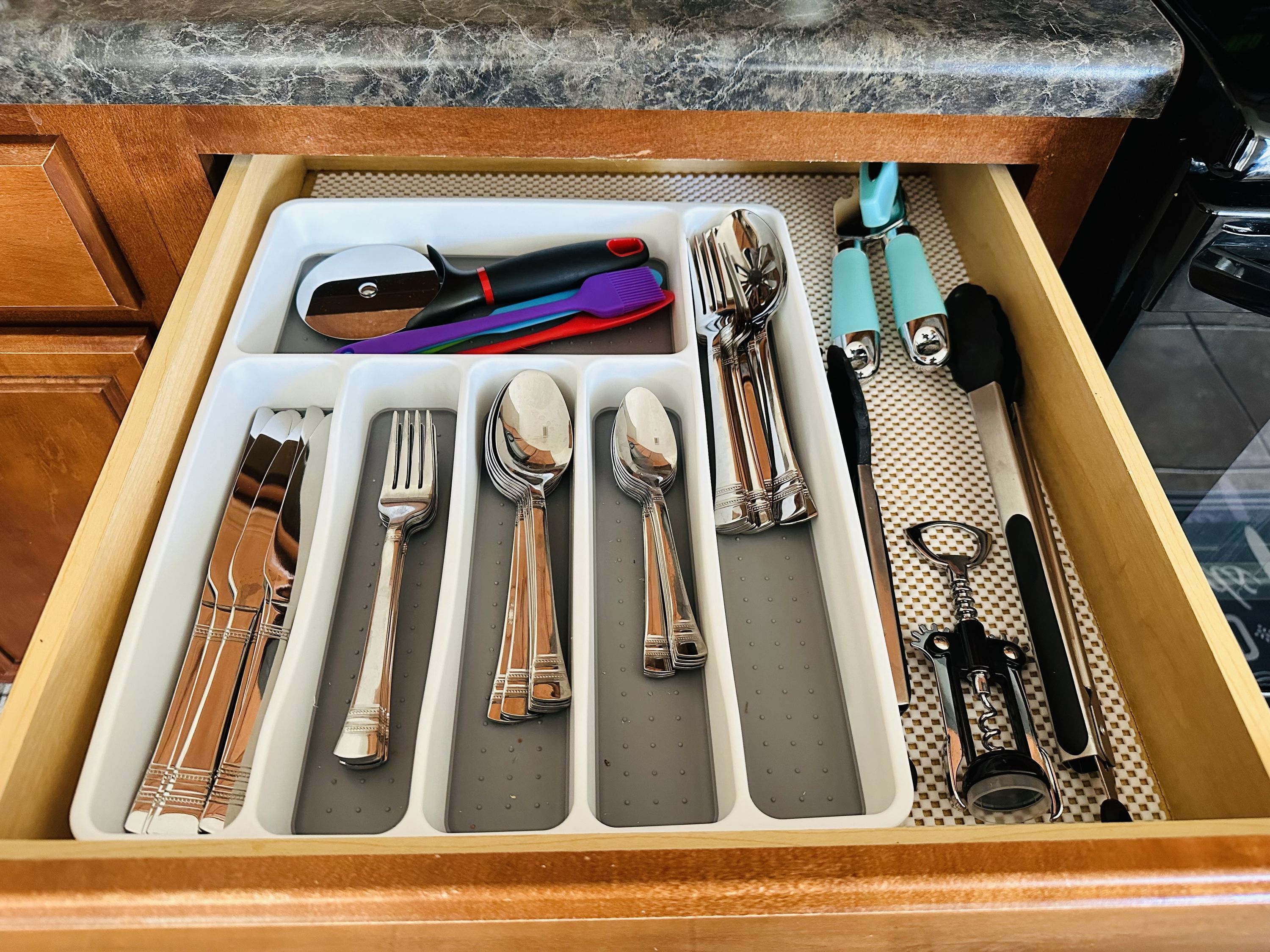 Un tiroir contenant des couverts soigneusement rangés, notamment des fourchettes, des cuillères et des couteaux, ainsi qu’une paire de ciseaux et un tire-bouchon.