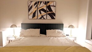 A large bed with a dark headboard, two bedside tables with lamps, and a yellow throw blanket. - 2756 Bridgegate Trce NE GA - Basement (Marietta)