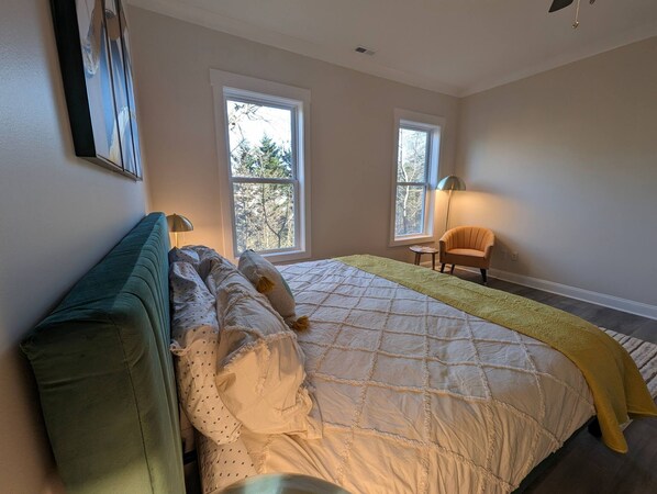 Une chambre avec un grand lit, deux fenêtres, une chaise et une lampe sur pied.