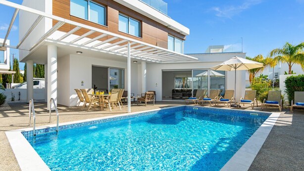 Ett modernt poolområde med en klarblå pool, solstolar och en överbyggd sittgrupp.