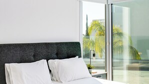 Ett modernt hotellrum med en stor säng, ett nattduksbord, ett skrivbord och utsikt över omgivningarna genom en glasdörr.