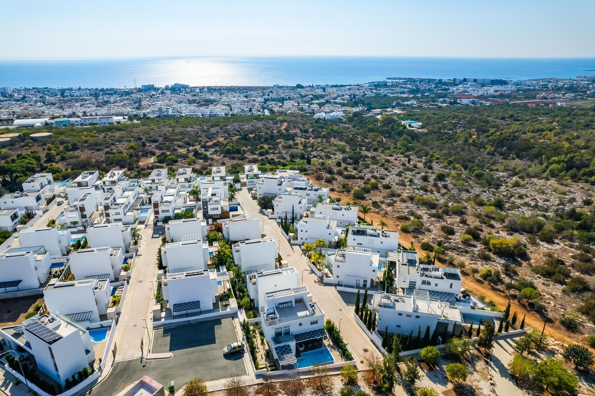 Una zona residencial costera con edificios blancos modernos, vista despejada del mar y una calle que atraviesa el vecindario.