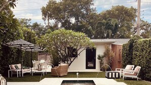 A rectangular swimming pool with a tiled edge, surrounded by a patio area with outdoor furniture and a pergola with string lights. - Charming Olde Naples Bungalow  (Naples)