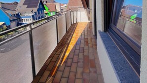 Een balkon met uitzicht op gebouwen, een betegelde vloer en een metalen hekwerk.