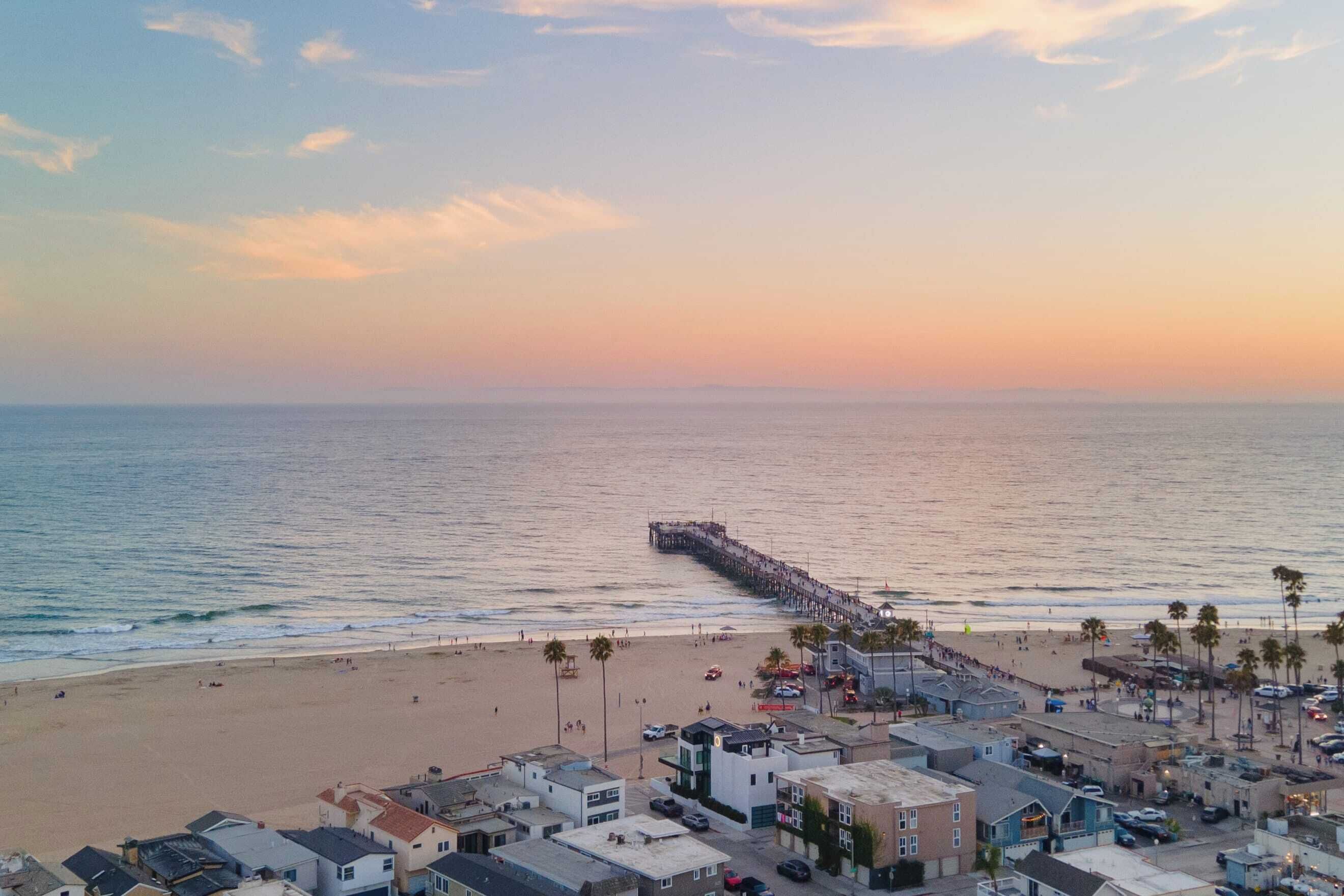 A coastal town with a pier extending into the sea, beachfront buildings, and palm trees.