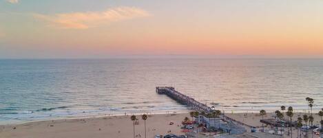 A coastal town with a pier extending into the sea, beachfront buildings, and palm trees.