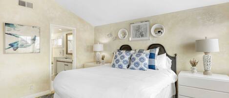 A bedroom with a large bed, two bedside tables with lamps, a dresser, and wall art.