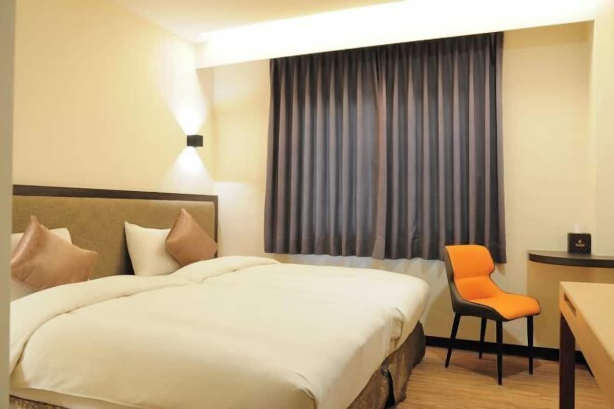 A hotel room with a bed, a chair, a desk, and a curtain.