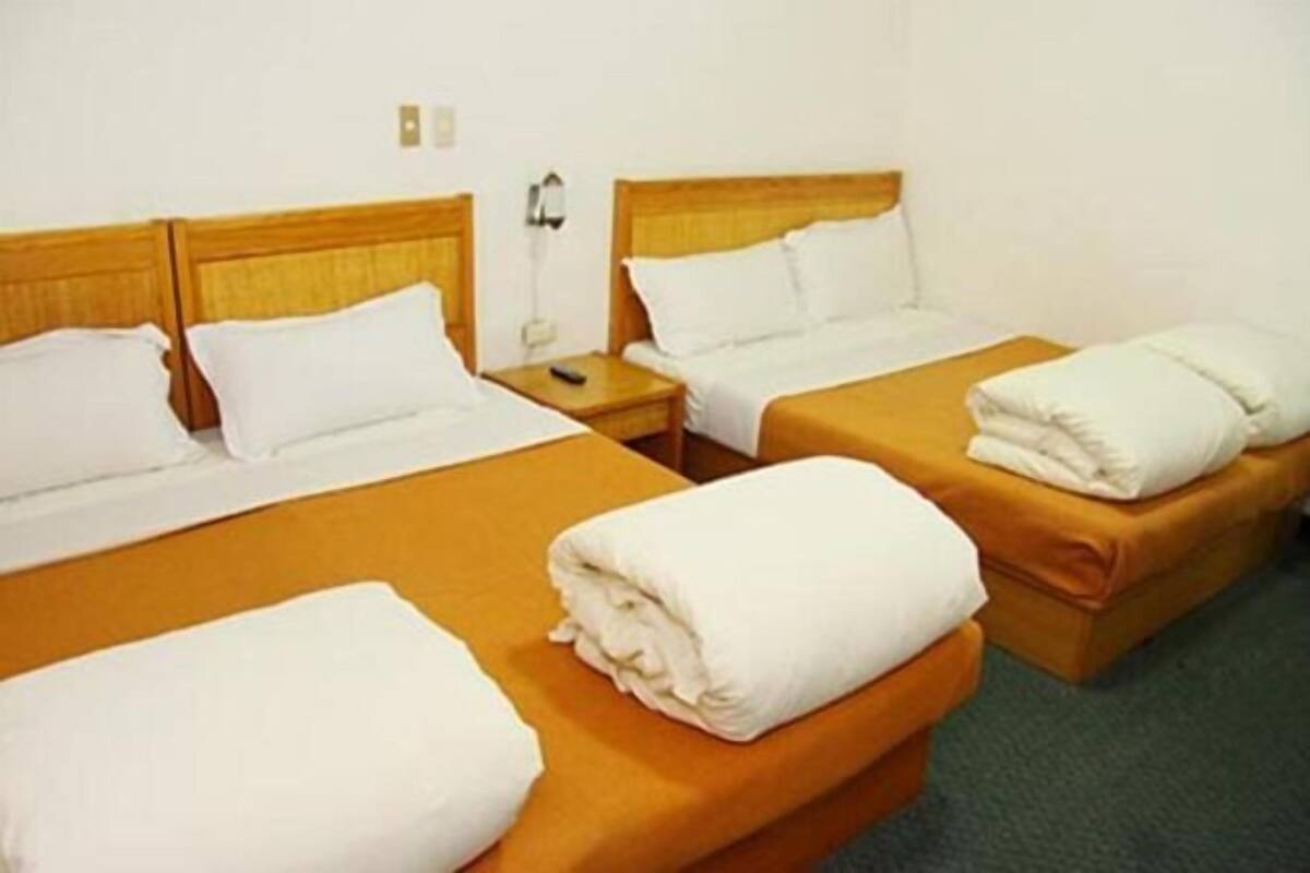A hotel room with two single beds, each with a wooden headboard and white bedding. There is a nightstand with a lamp and a folded towel on the bed.