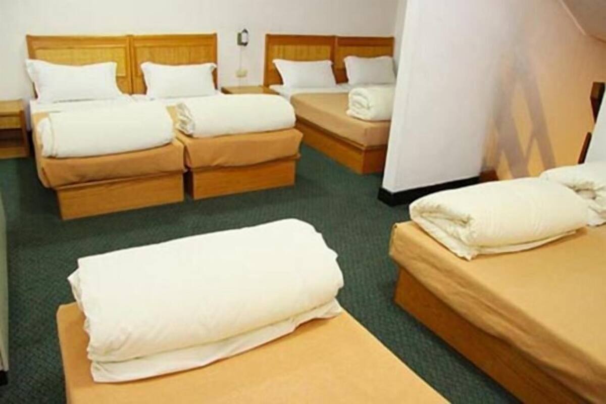 A hotel room with two single beds and one double bed, all with white linens.