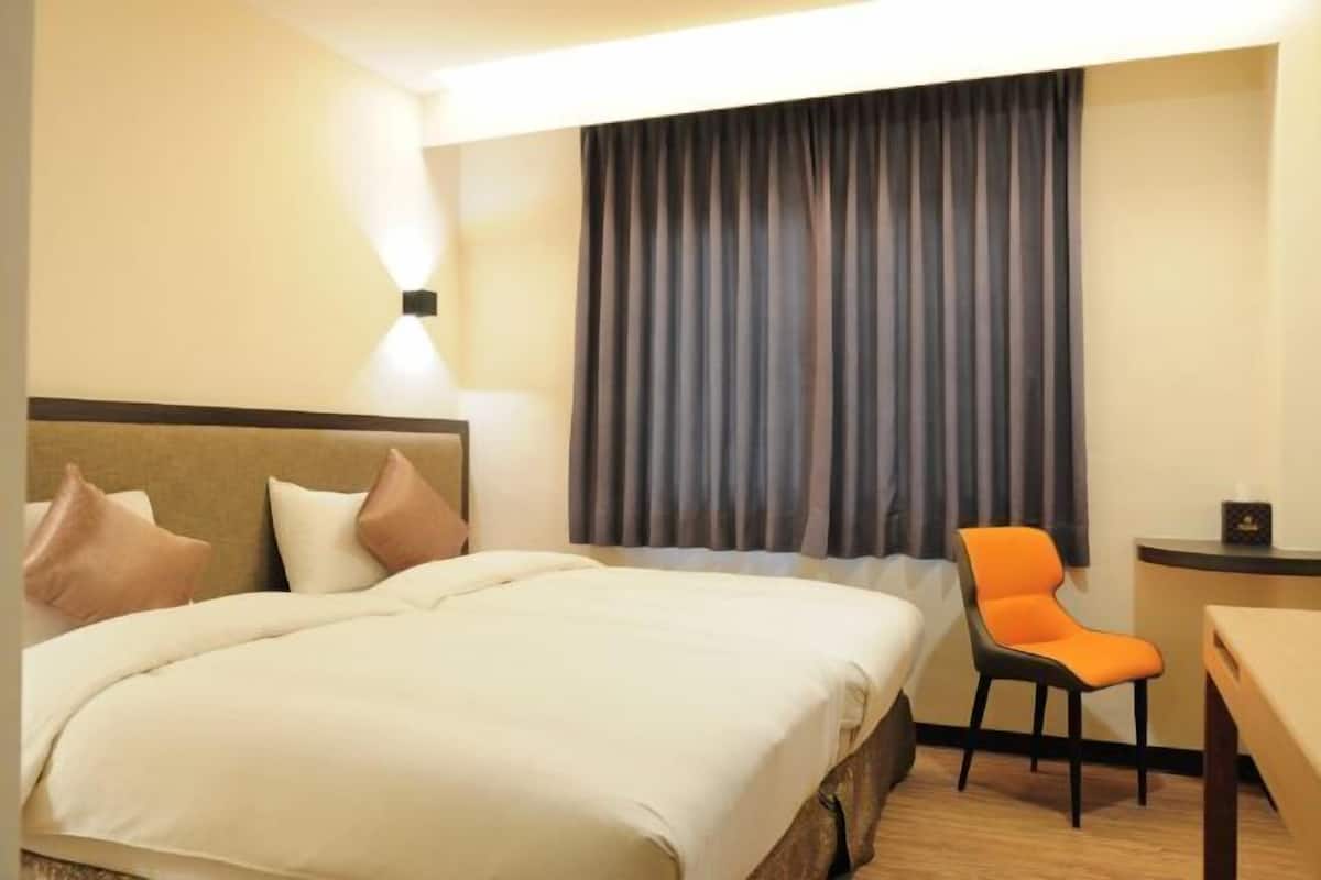 A hotel room with a bed, a desk, a chair, and a large window with curtains.