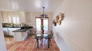 A kitchen with white cabinets, a black countertop, and a dining area with a glass table and chairs. - Charming 2-bedroom house with WiFi, AC in welcoming Yucca Valley (Yucca Valley)
