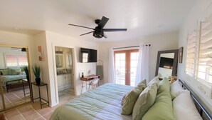 A bedroom with a bed, a desk, a chair, a ceiling fan, and a large window with curtains. - Charming 2-bedroom house with WiFi, AC in welcoming Yucca Valley (Yucca Valley)