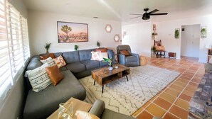 A spacious living room with a grey sofa, a wooden coffee table, and a ceiling fan. - Charming 2-bedroom house with WiFi, AC in welcoming Yucca Valley (Yucca Valley)