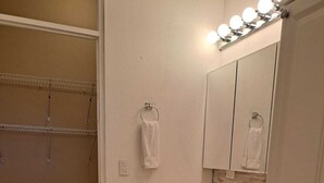 Un baño con tocador, espejo con luces, barra de toallas y papel tapiz estampado.