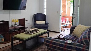 Una sala de estar con televisor de pantalla plana, ventilador de techo, sofá, sillón y mesa de centro.
