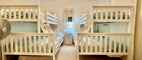 A room with two bunk beds, a ceiling fan, a nightstand, and a mirror.
