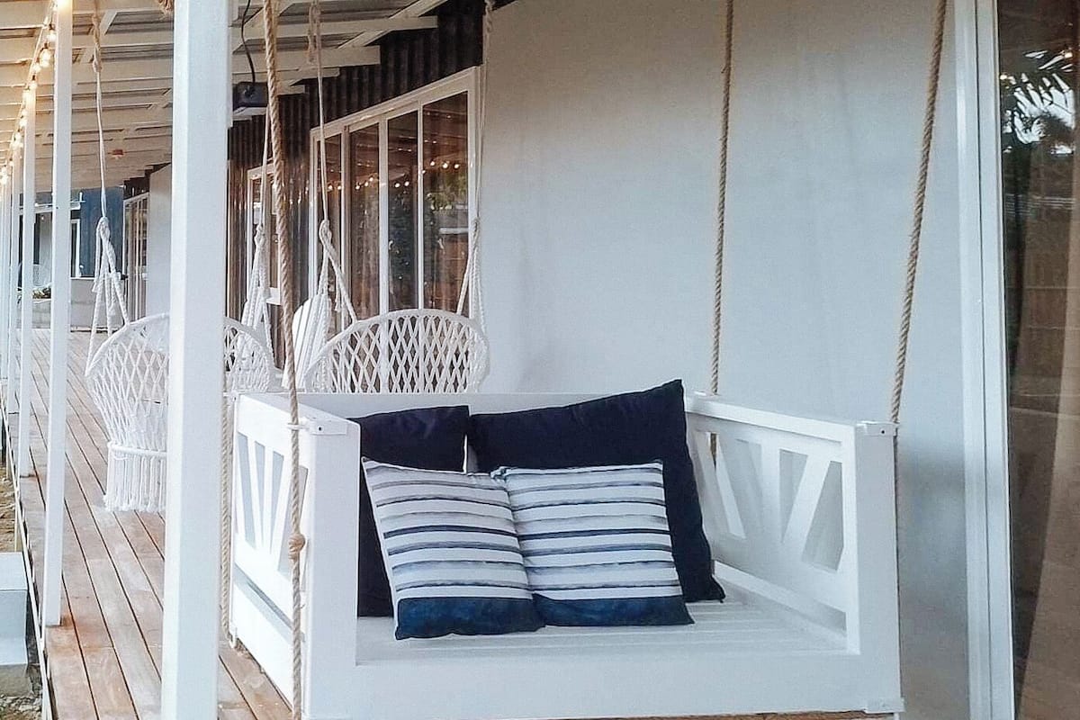 Una silla mecedora blanca con cojines a rayas sobre una terraza de madera.