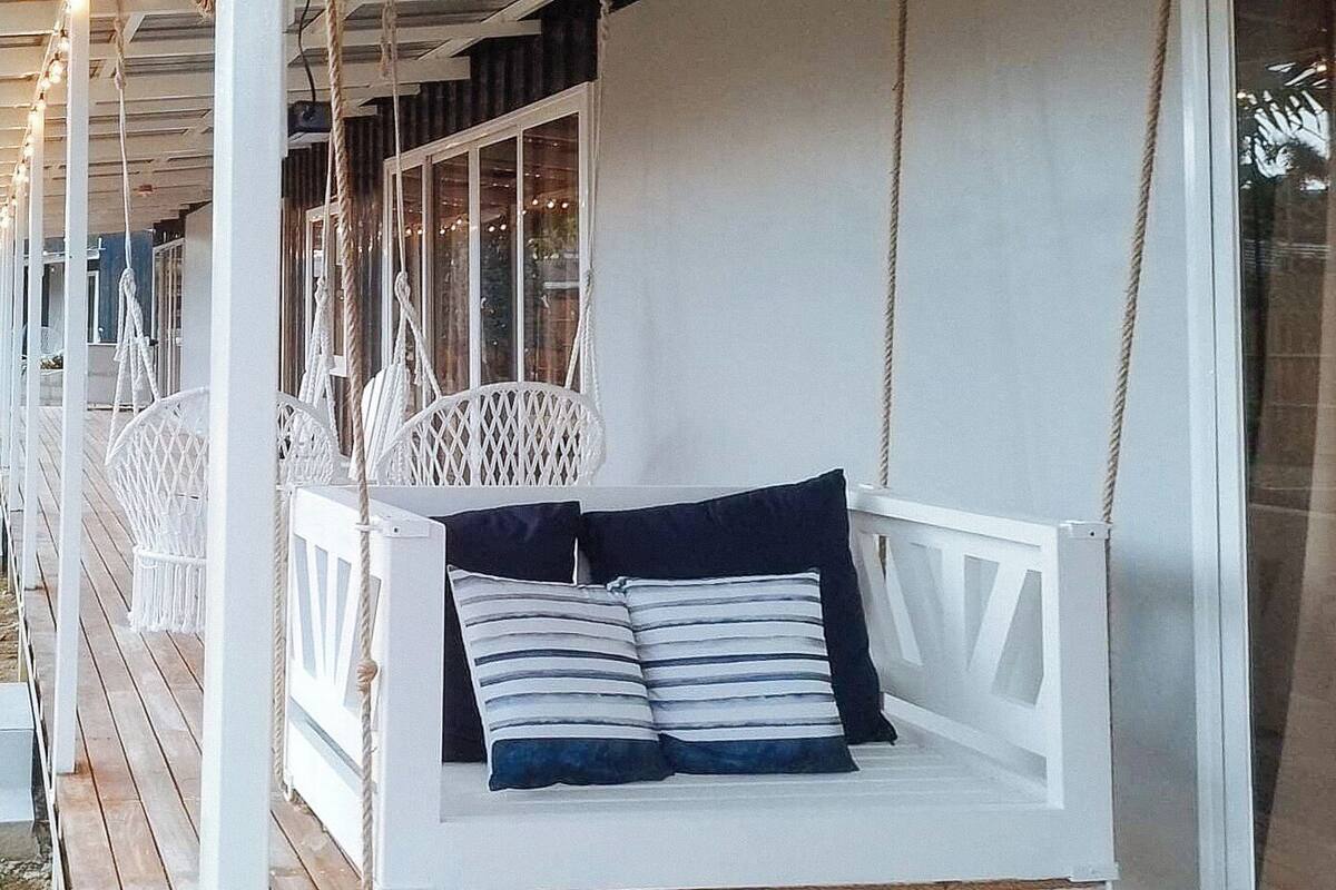 A white swing chair with striped cushions on a wooden deck.