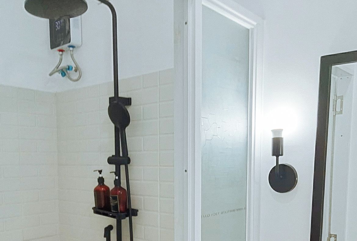 Un baño con ducha, inodoro y lavamanos. Hay dos botellas en la repisa del lavamanos.