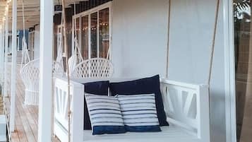 A white swing chair with striped cushions on a wooden deck.