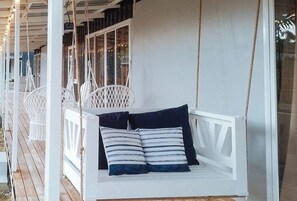 A white swing chair with striped cushions on a wooden deck. - Angels Bed And Breakfast Sipalay City By Reddoorz (Sipalay)