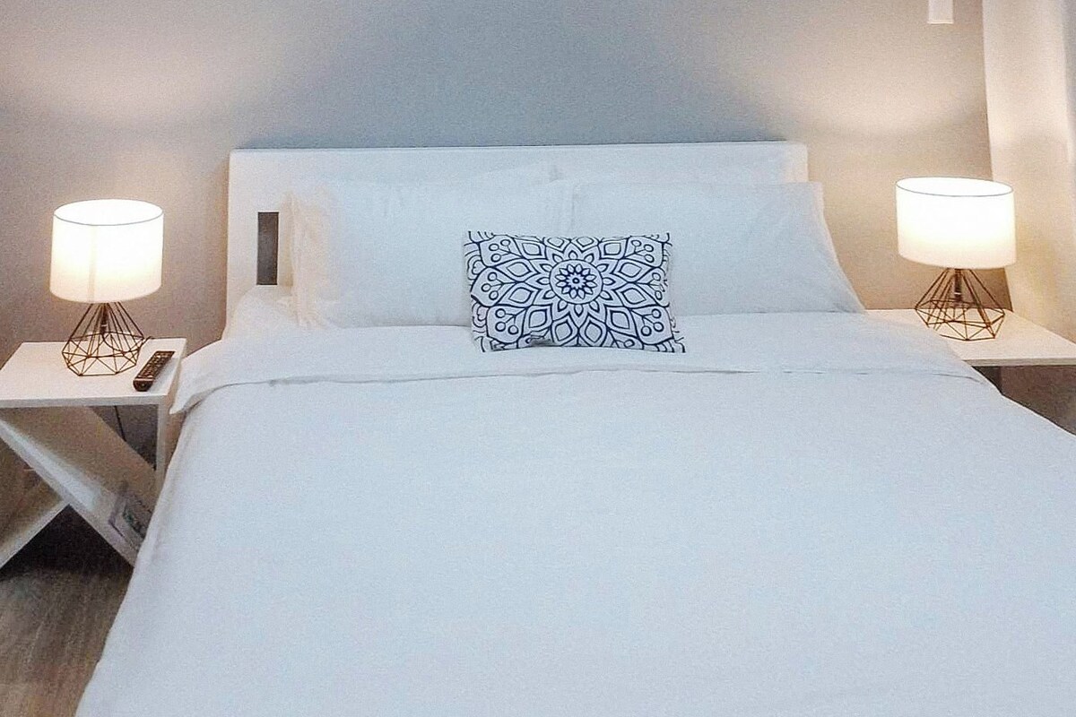 A neatly made bed with white linens, a patterned pillow, and two bedside tables with lamps.