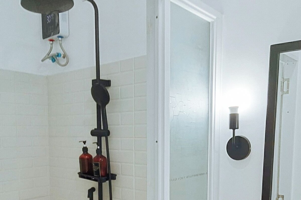 A bathroom with a shower, a toilet, and a sink. There are two bottles on the sink's shelf.