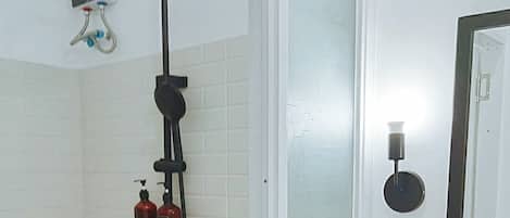 Un baño con ducha, inodoro y lavamanos. Hay dos botellas en la repisa del lavamanos.