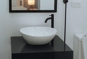A white vessel sink on a black countertop with a black faucet, a mirror above it, and a white wall with a power outlet. - Angels Bed And Breakfast Sipalay City By Reddoorz (Sipalay)
