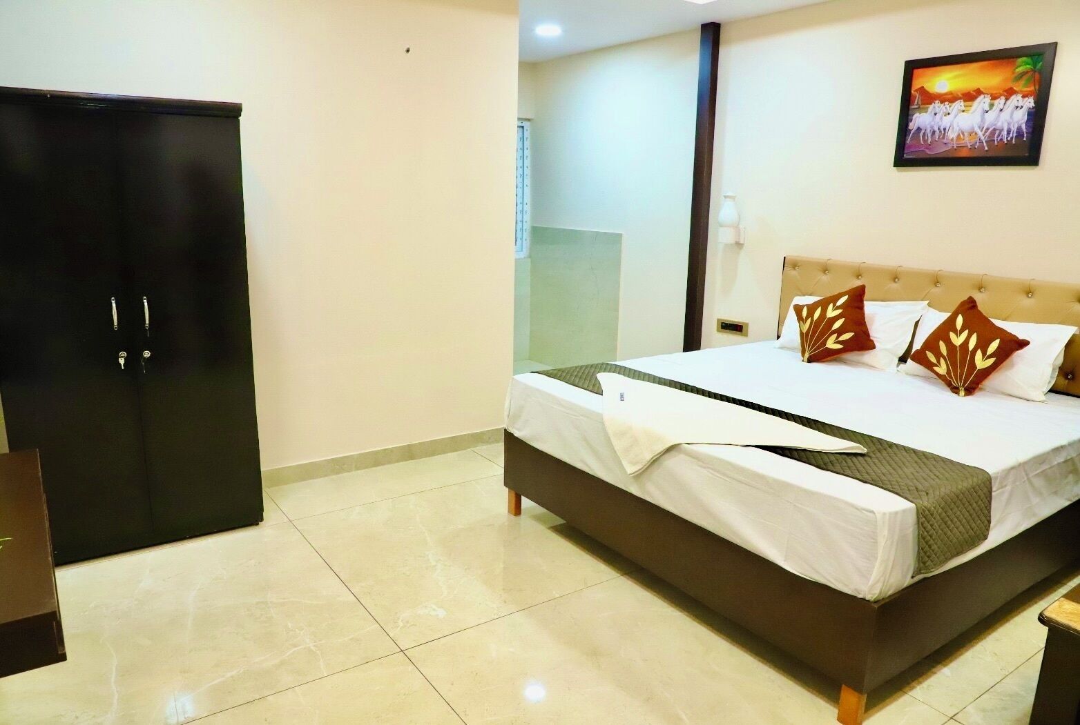 A hotel room with a bed, a wardrobe, a painting on the wall, and a tiled floor.