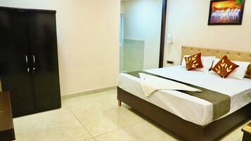 A hotel room with a bed, a wardrobe, a painting on the wall, and a tiled floor.