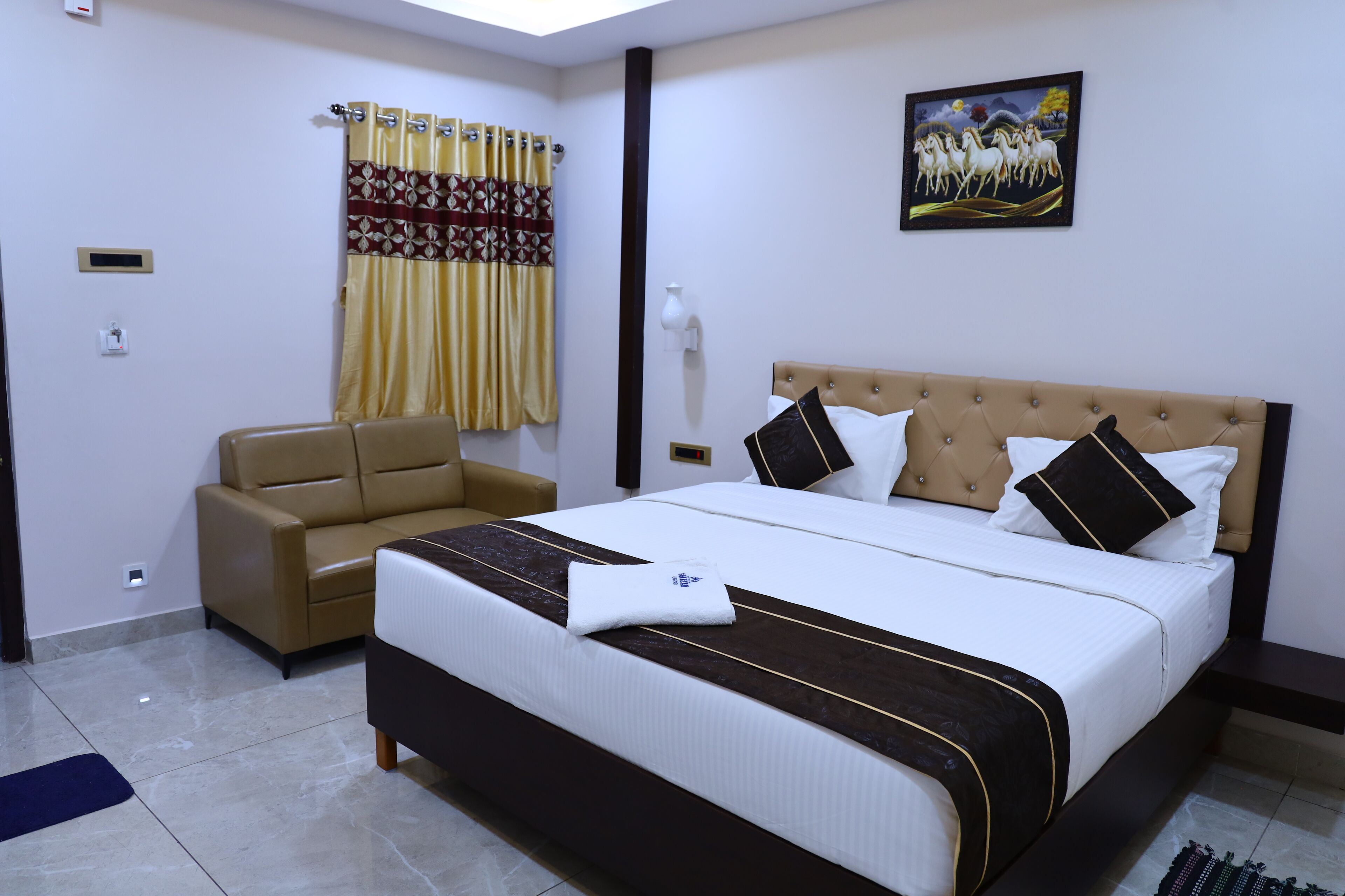 A hotel room with a large bed, a sofa, a painting on the wall, and a window with curtains.